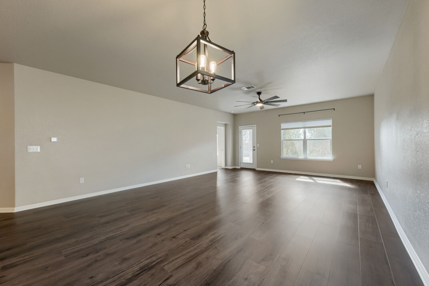 Rich wood-look flooring stretches across a spacious, open living area beneath high ceilings.