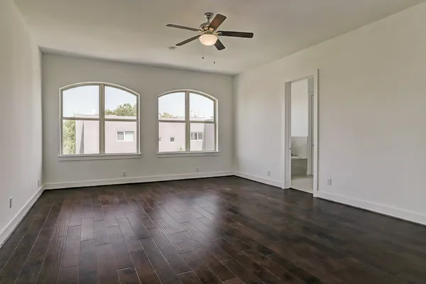 an empty room with wooden floor chandelier fan and windows