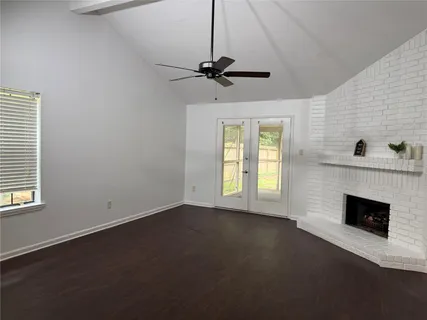 a view of an empty room with wooden floor fireplace and a window