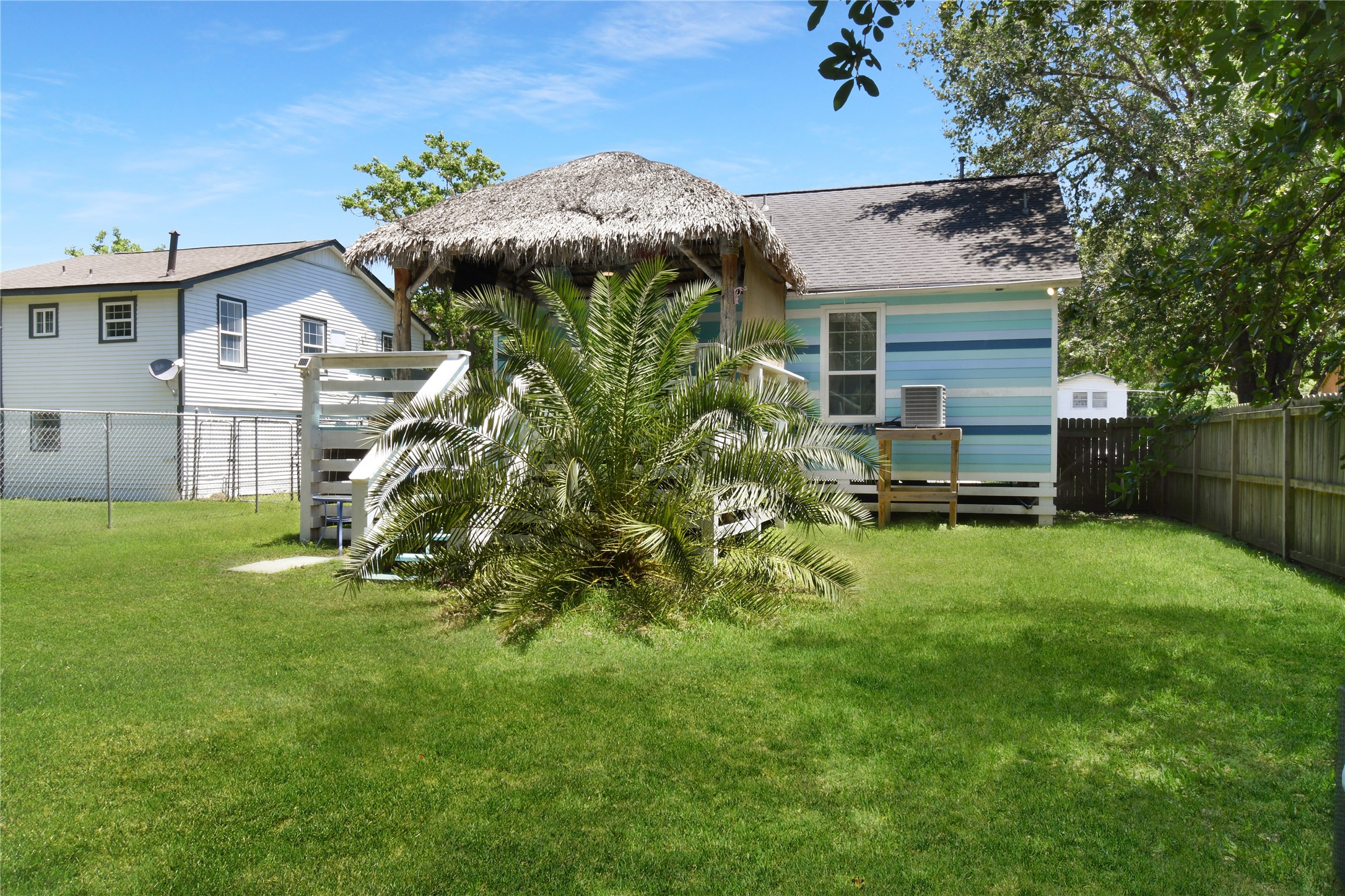 320 10th Street Dickinson, TX 77539 - Photo 3 of 21 Discover the perfect oasis in this inviting backyard, featuring lush greenery, a charming thatched-roof deck, and vibrant blue accents that create a serene, tropical retreat.