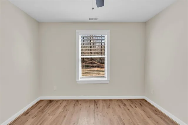 an empty room with wooden floor ceiling fan and windows