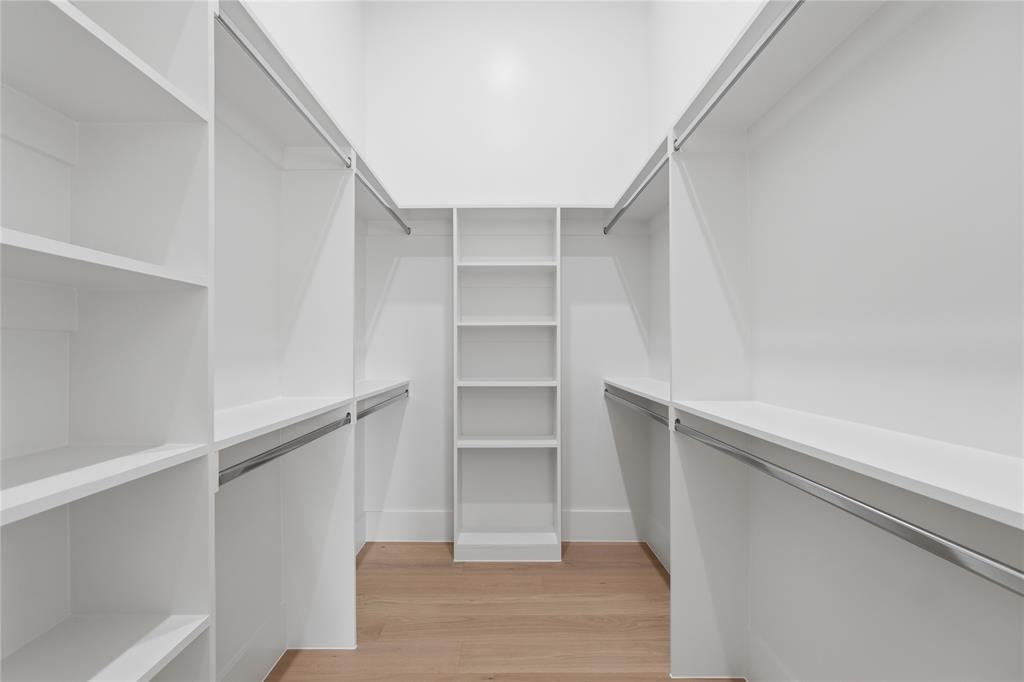 6038 Prospect Avenue Dallas, TX 75206 - Photo 20 of 40 Walk-in closet featuring extensive built-in shelving, multiple hanging rods, warm wood-finish flooring, and crisp white walls