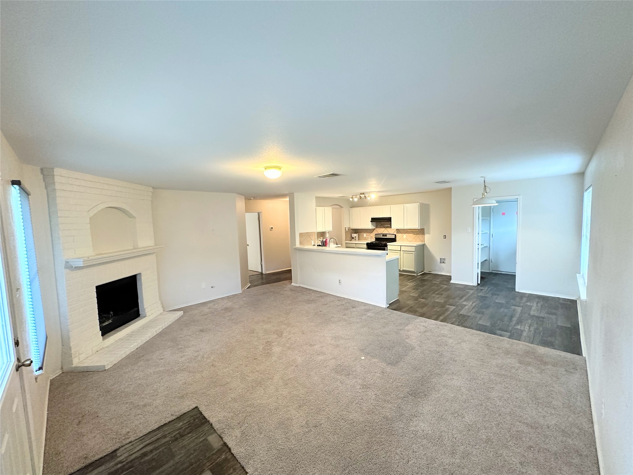 12929 Waynespur Lane Elgin, TX 78621 - Photo 19 of 20 The living area features a white brick fireplace, carpeted flooring, and a kitchen area with white cabinetry and dark appliances