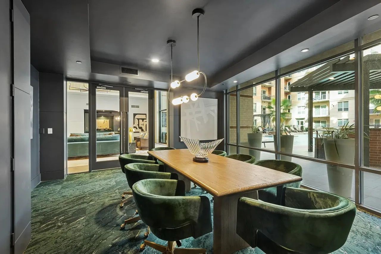 2724 Kipling Street, Unit 504 Houston, TX 77098 - Photo 2 of 30 This conference room space is anchored by a sleek, natural wood table, surrounded by plush, velvet-upholstered chairs in a rich green tone that adds warmth and elegance.