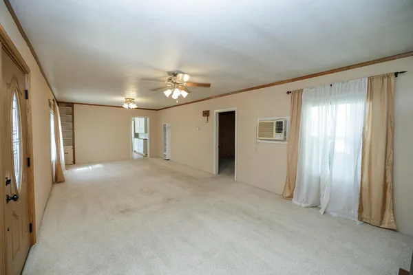 an empty room with chandelier fan and windows