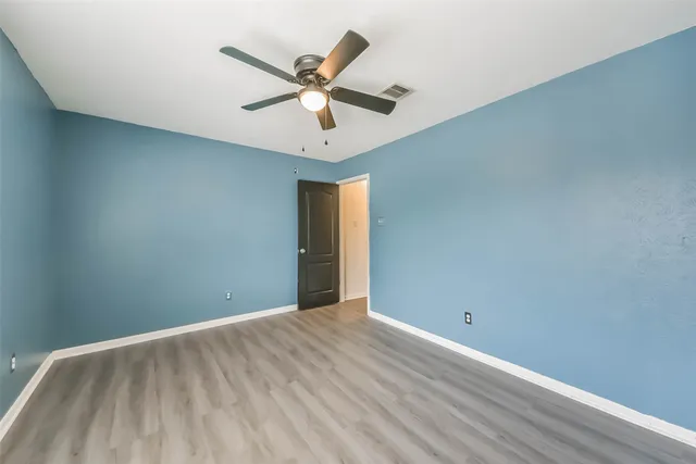 an empty room with wooden floor fan and windows