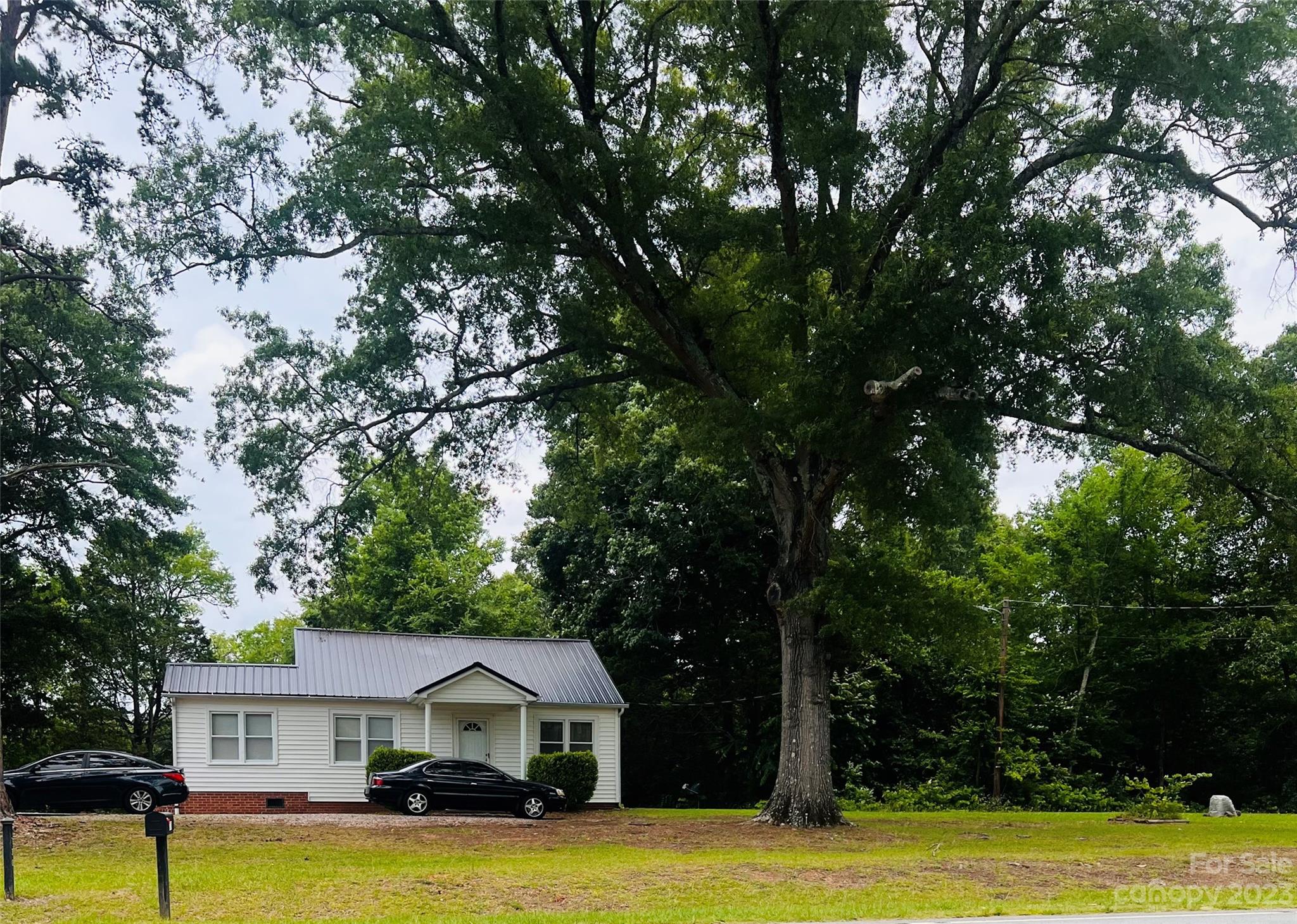 a view of a white house in a big yard with large trees
