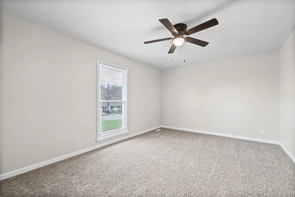 an empty room with ceiling fan and windows