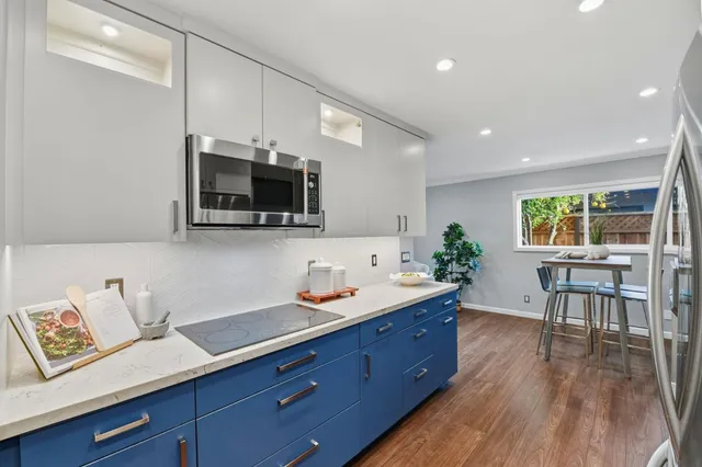 a kitchen with stainless steel appliances kitchen island granite countertop a sink a stove a dining table and chairs with wooden floor