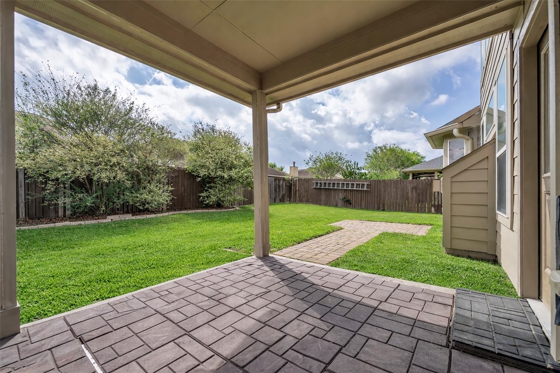 1230 Maple Ace Drive Katy, TX 77493 - Photo 37 of 40 This photo showcases a charming backyard with a covered patio area, paved pathway, and lush green lawn, bordered by a wooden fence and mature shrubs for privacy.