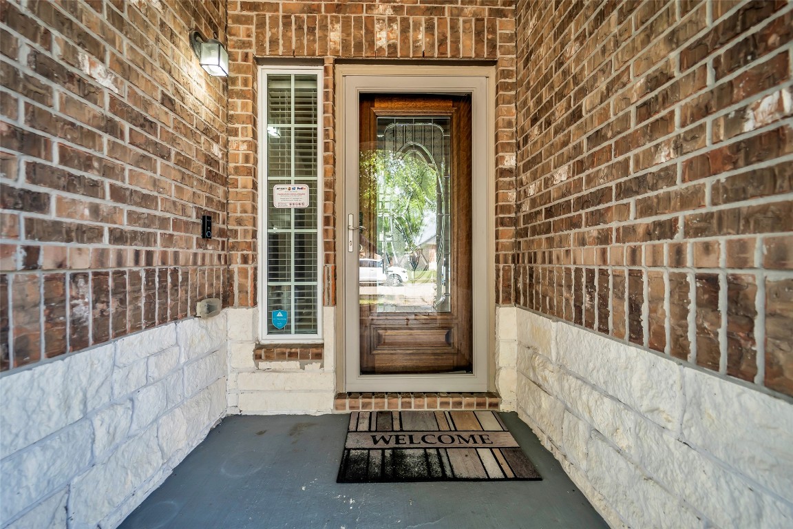 1230 Maple Ace Drive Katy, TX 77493 - Photo 4 of 40 This inviting entryway features a welcoming glass-paneled door, framed by a mix of brick and stonework. A side window enhances natural light, and a "Welcome" mat adds a homey touch.