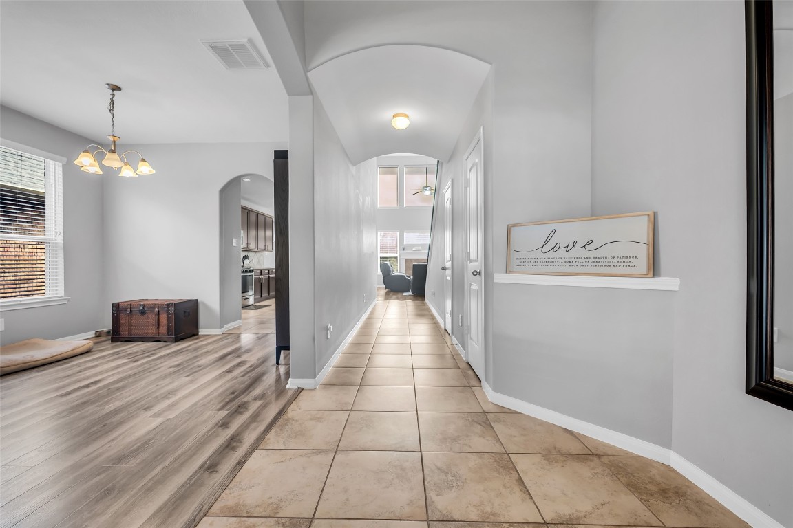 1230 Maple Ace Drive Katy, TX 77493 - Photo 5 of 40 This photo showcases a bright, welcoming hallway with tiled flooring, archways, and a view into a living area. To the left, there's a cozy living & dining combo space with wood flooring and ample natural light from large windows. The walls are painted in a soft gray, enhancing the modern, airy feel.
