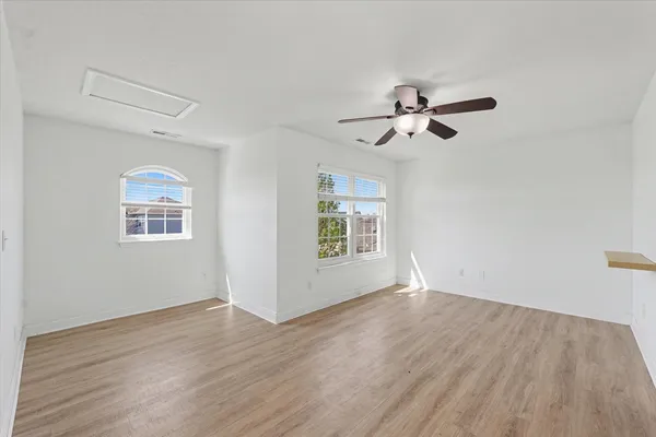 an empty room with wooden floor chandelier fan and windows