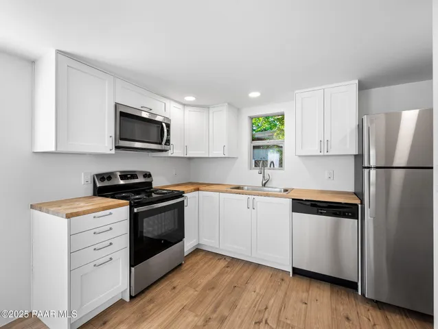 a kitchen with stainless steel appliances granite countertop a refrigerator a stove top oven a sink and dishwasher with wooden floor