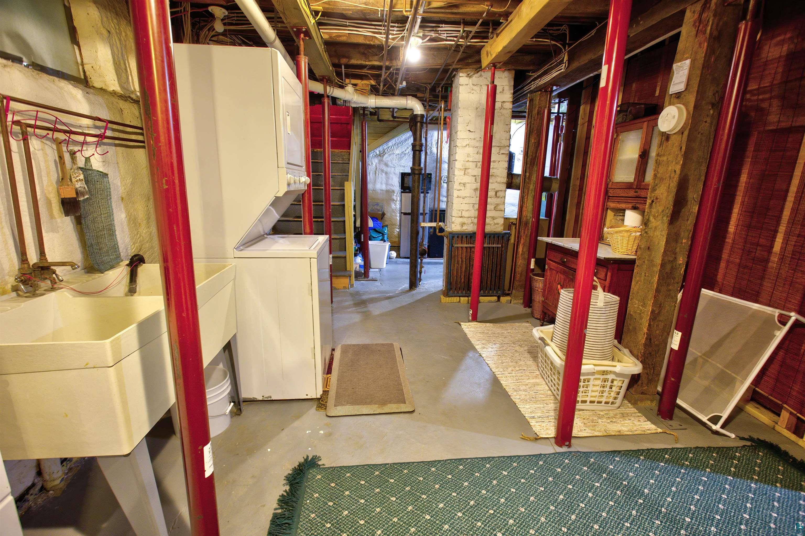 24 East Conan Street Ely, MN 55731 - Photo 25 of 27 Laundry area featuring a utility sink, a stacked washer and dryer, and exposed structural beams