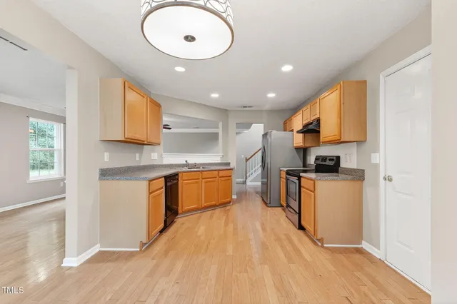 a large kitchen with stainless steel appliances granite countertop a stove a sink a refrigerator and white cabinets with wooden floor