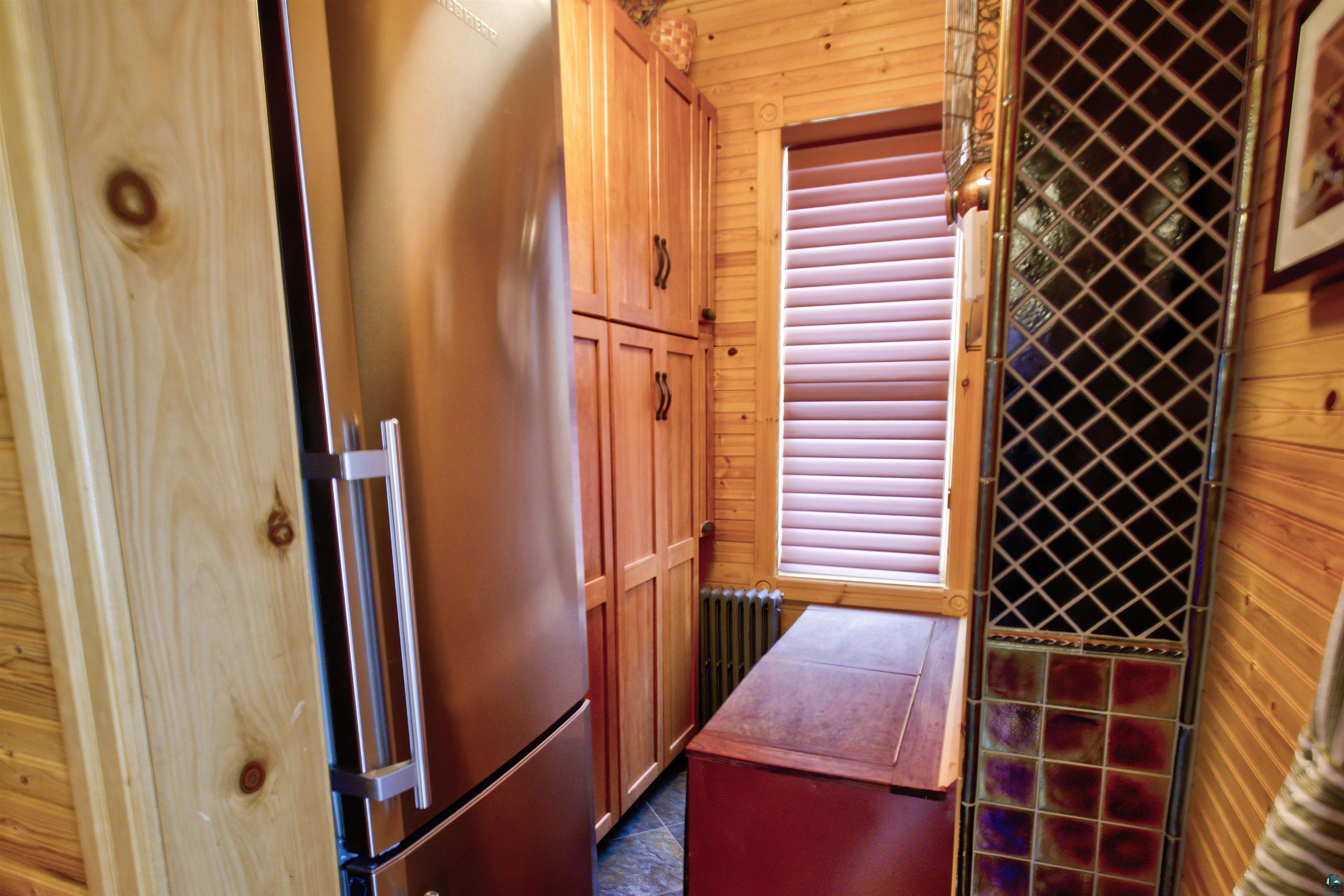 24 East Conan Street Ely, MN 55731 - Photo 12 of 27 Stainless steel refrigerator, custom built-in cabinetry, wood paneling, window with horizontal blinds, and a decorative stained glass panel