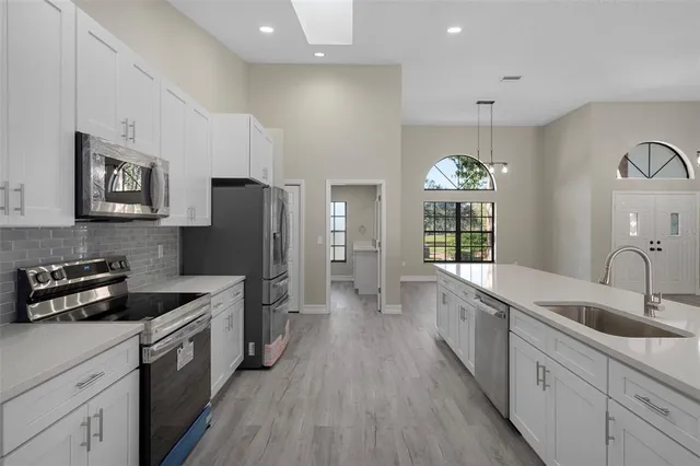 a large kitchen with stainless steel appliances a sink cabinets and a wooden floor