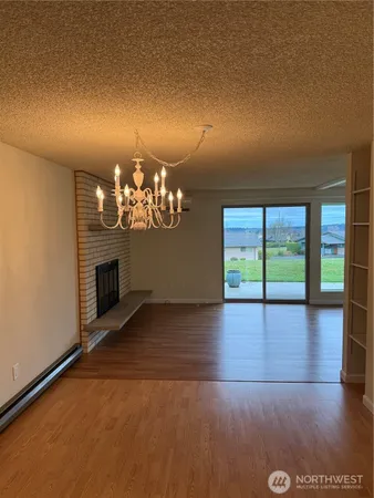 an empty room with wooden floor fireplace and chandelier
