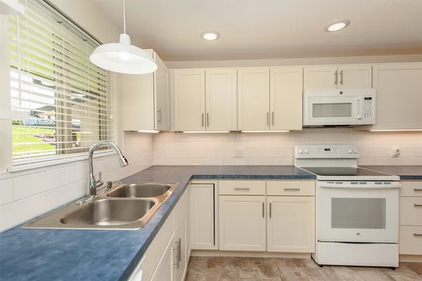 a kitchen with granite countertop a sink dishwasher a stove and white cabinets with wooden floor