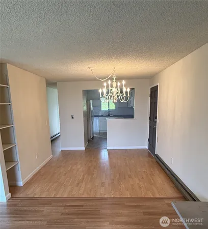 an empty room with wooden floor and kitchen view