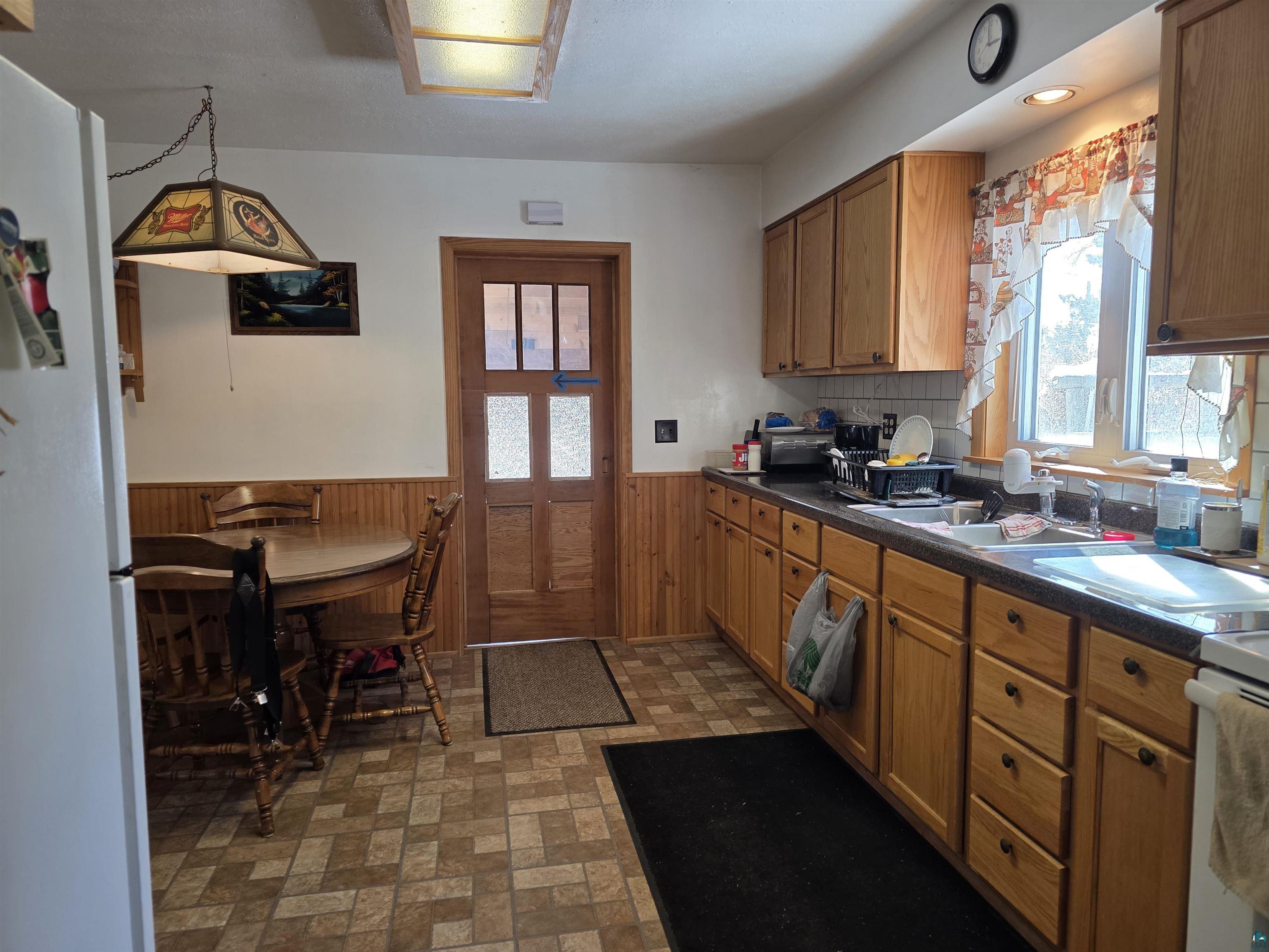 406 North Road Cloquet, MN 55720 - Photo 8 of 26 Kitchen with white appliances, dark countertops, a wainscoted wall, brick patterned flooring, and wooden walls