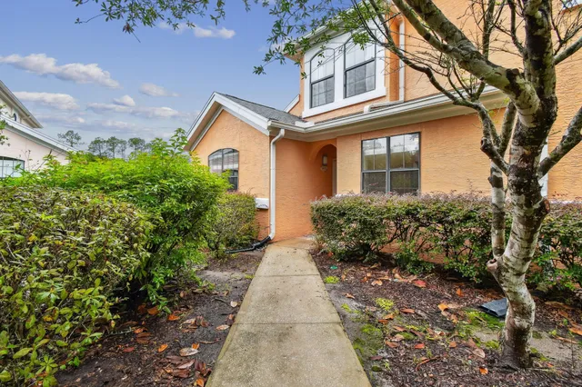 a view of a brick house with large windows and a yard with plants and large trees