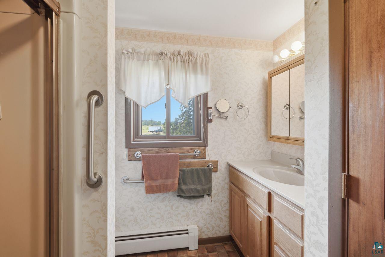 61018 Dahlstrom Road Ashland, WI 54806 - Photo 14 of 28 Full bathroom featuring a shower with grab bar, single vanity with wood-finish cabinetry, built-in medicine cabinet, and a window with exterior scenery