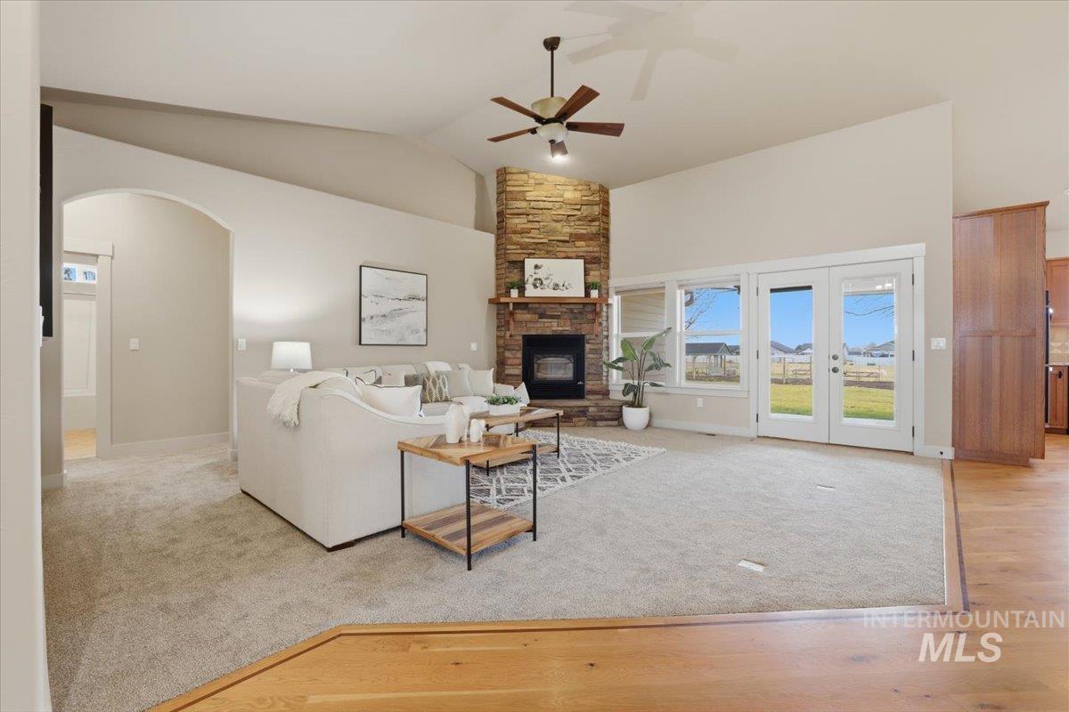 Living room featuring ceiling fan, light colored carpet, vaulted ceiling, a stone fireplace, and arched walkways