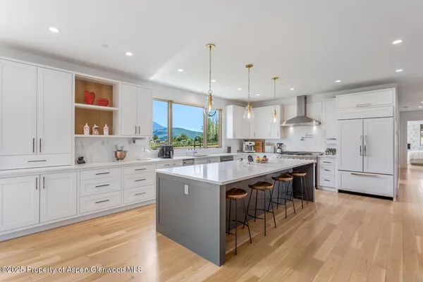 a large kitchen with stainless steel appliances kitchen island granite countertop a stove a sink a refrigerator and white cabinets with wooden floor