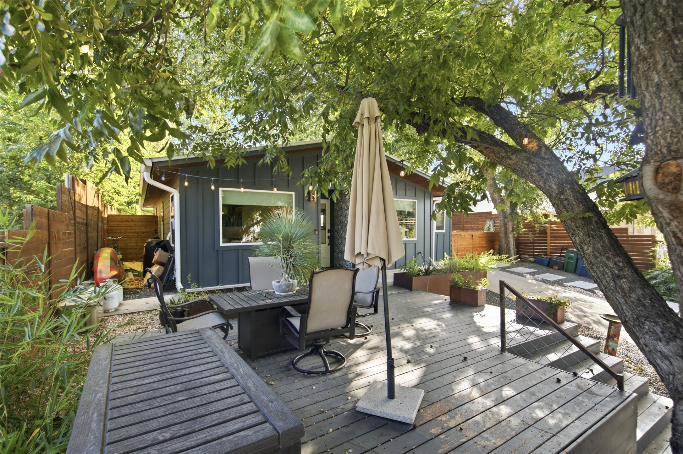 5600 Ledesma Road Austin, TX 78721 - Photo 18 of 36 Mature trees shade a spacious wooden deck positioned behind a modern board-and-batten home.
