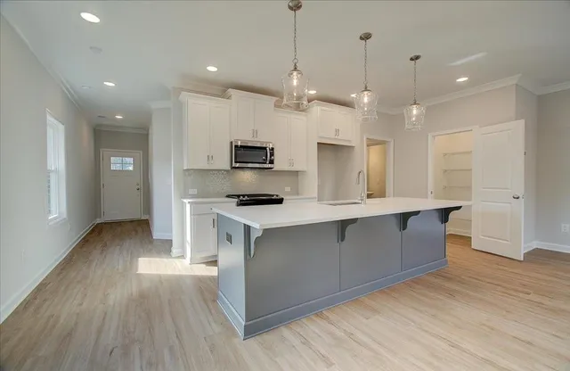 a large kitchen with stainless steel appliances a large counter top a stove a sink a refrigerator and a wooden floor