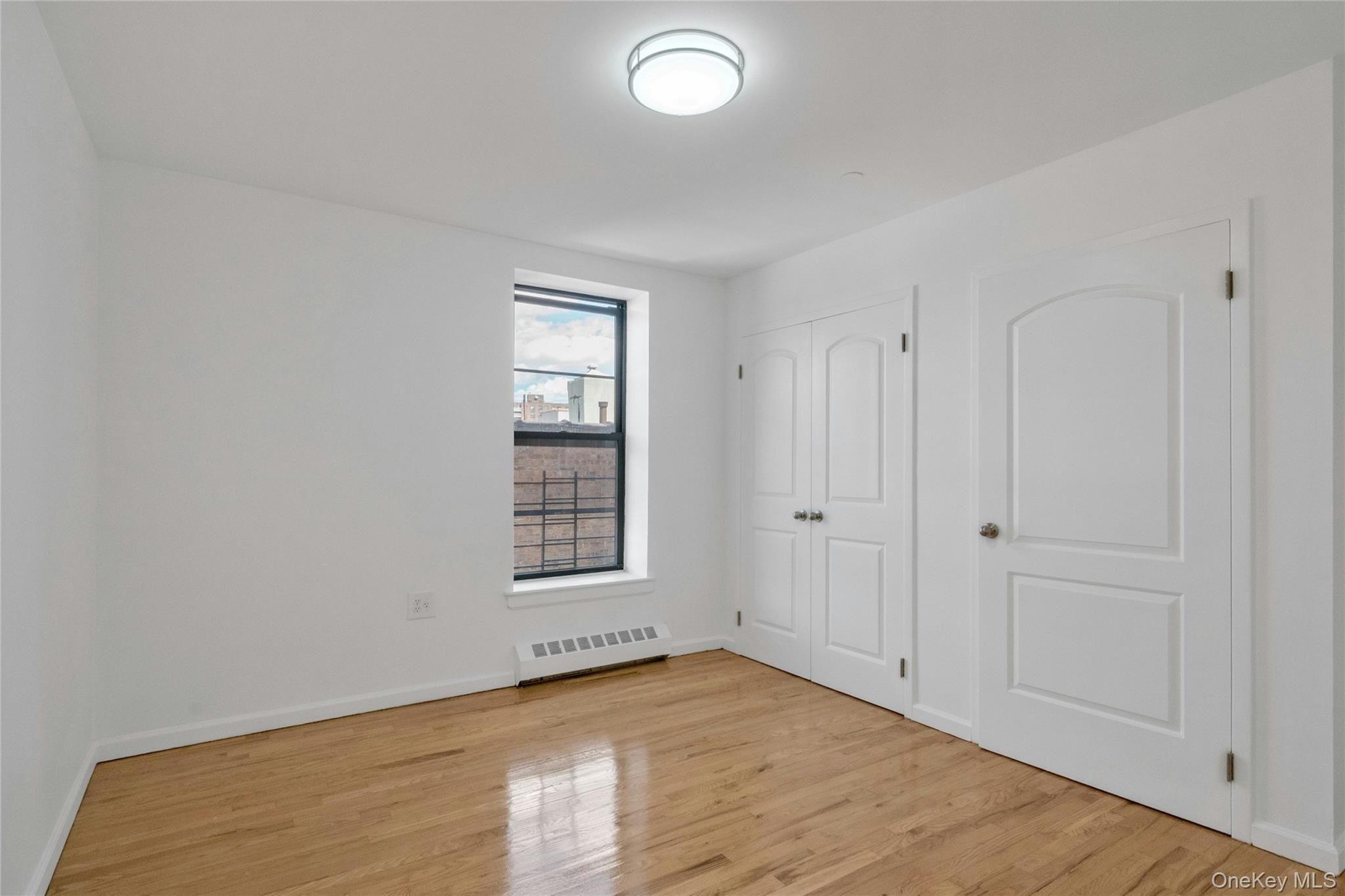 2023 Belmont Avenue, Unit 5A Bronx, NY 10457 - Photo 12 of 19 an empty room with wooden floor and windows