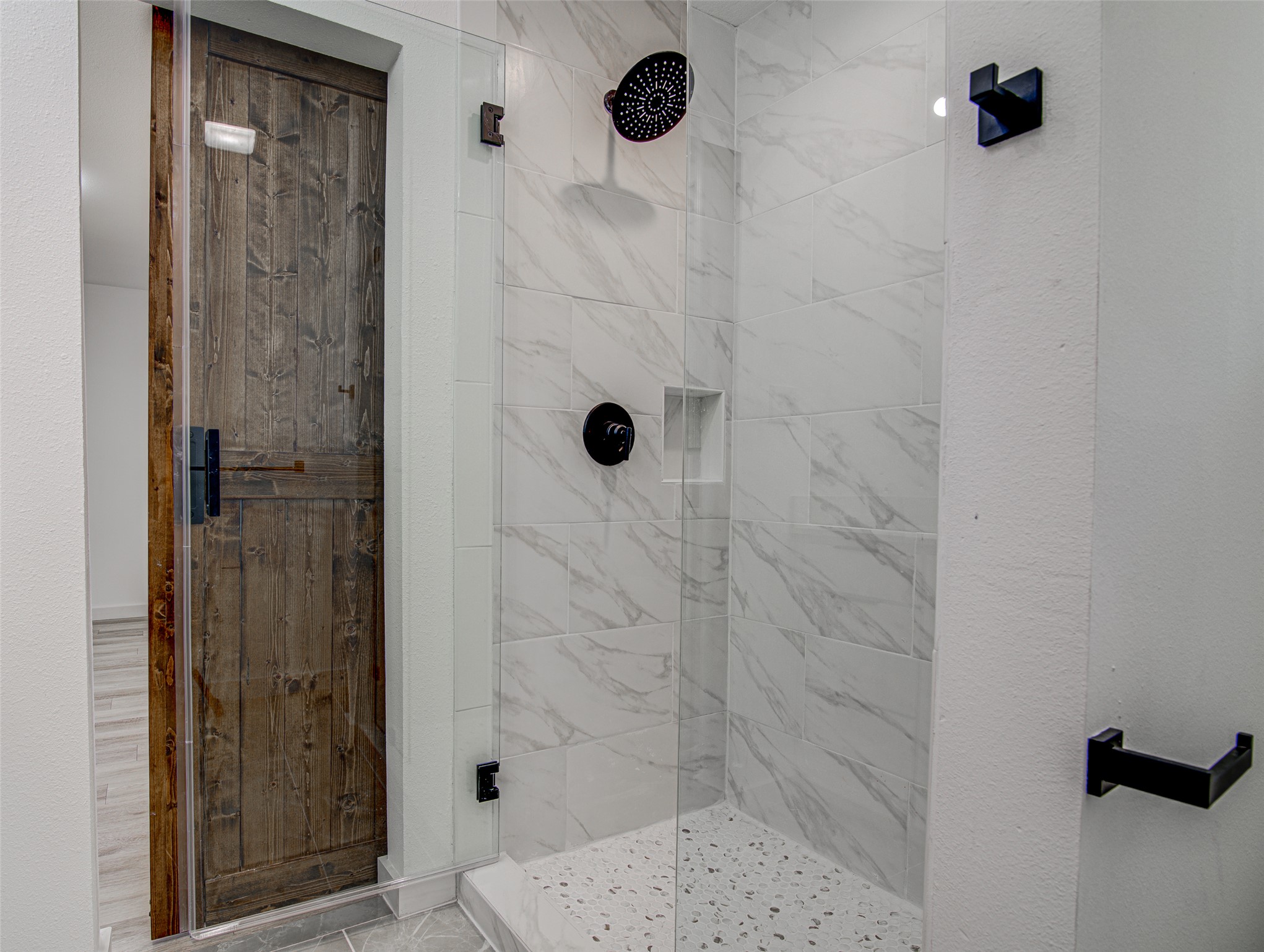 207 Haley Road Johnson City, TX 78636 - Photo 16 of 31 A sleek, contemporary shower with elegant marble-patterned tile and a dark wood door.