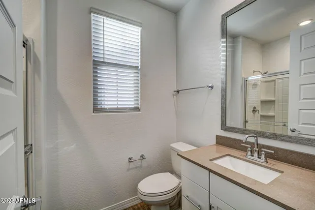 a bathroom with a granite countertop toilet a sink a mirror and a window