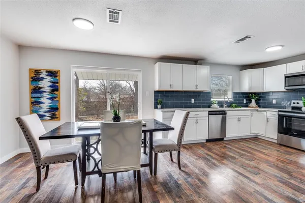 a kitchen with a table chairs a sink dishwasher a refrigerator and cabinets with wooden floor