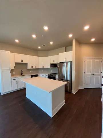 a large white kitchen with kitchen island granite countertop a stove top oven and a refrigerator with wooden floor
