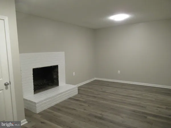 a view of an empty room with wooden floor and a fireplace
