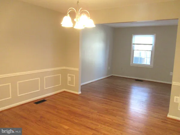 an empty room with wooden floor chandelier and windows