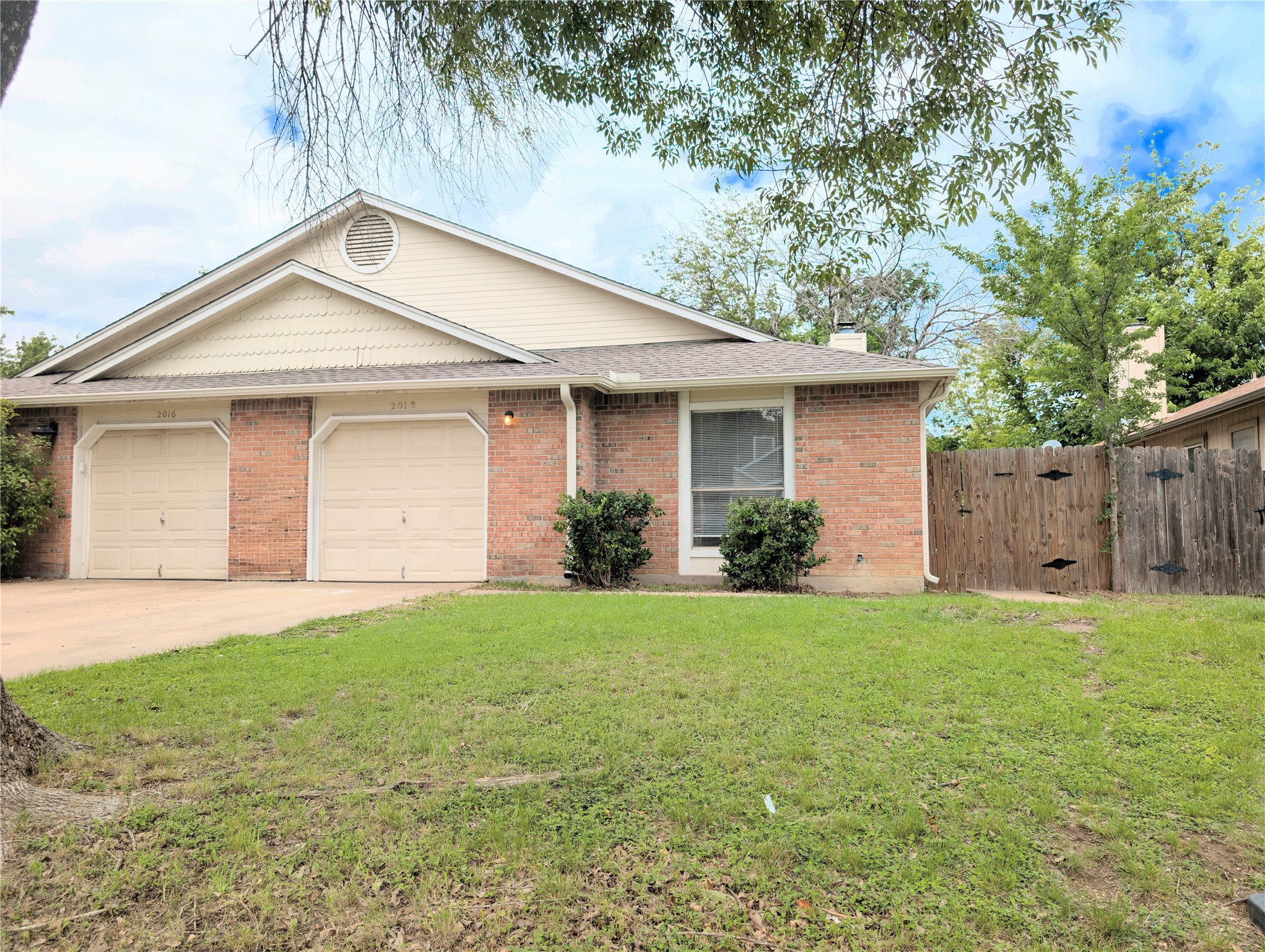 Brick facade property featuring two garage doors, a single window, and a wooden privacy fence