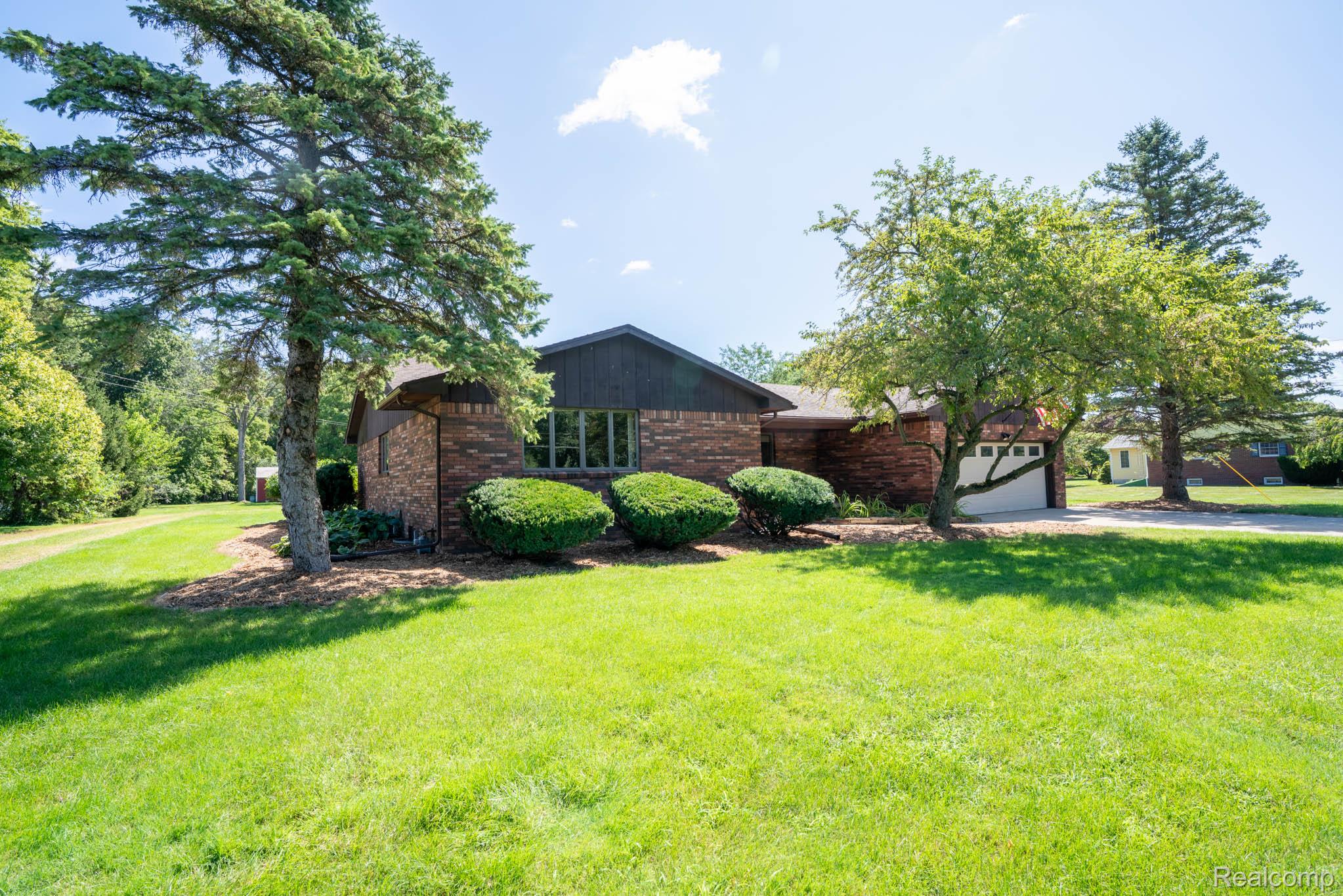 12900 Maxwell Road Carleton, MI 48117 - Photo 16 of 59 Brick exterior with dark siding accents, attached garage, mature trees, and landscaped shrubbery