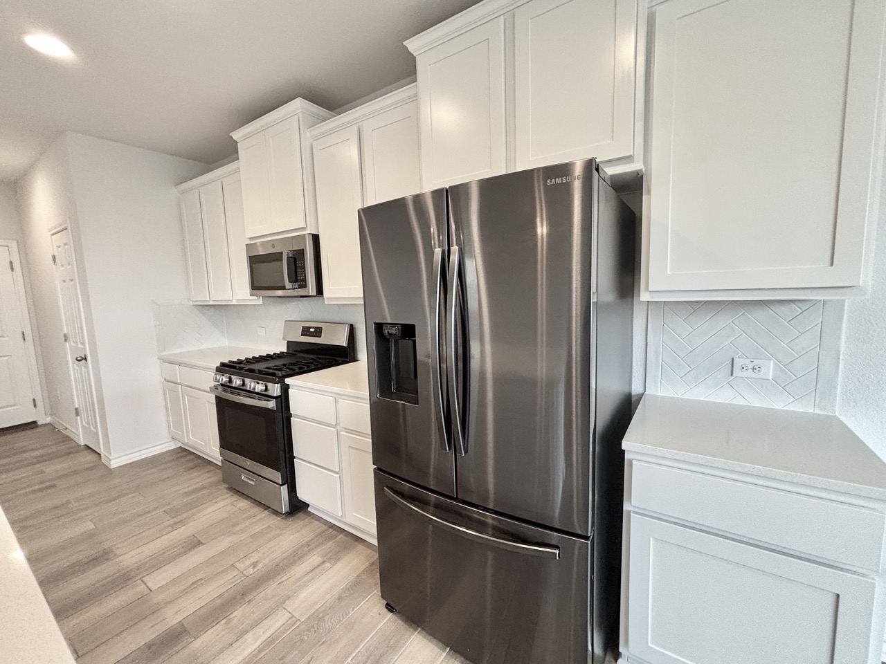 7606 Elk Grove Path Austin, TX 78754 - Photo 9 of 40 Kitchen with stainless steel appliances, white cabinets, decorative backsplash, light wood-style flooring, and recessed lighting