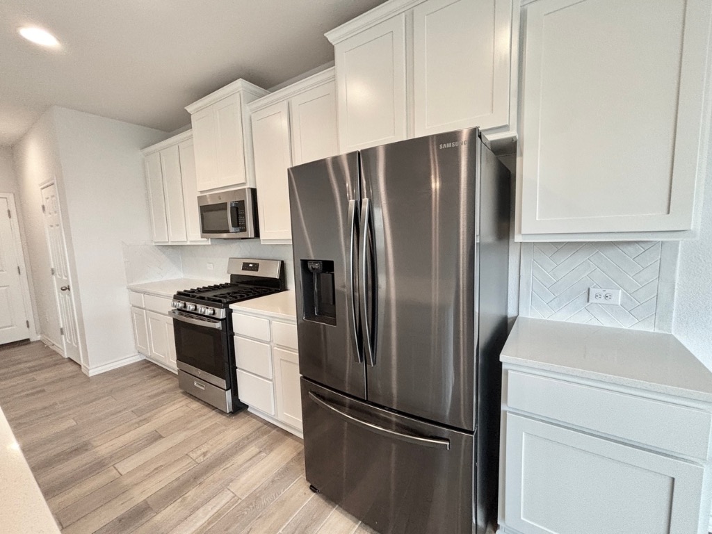 7606 Elk Grove Path Austin, TX 78653 - Photo 9 of 40 Kitchen with stainless steel appliances, white cabinets, decorative backsplash, light wood-style flooring, and recessed lighting