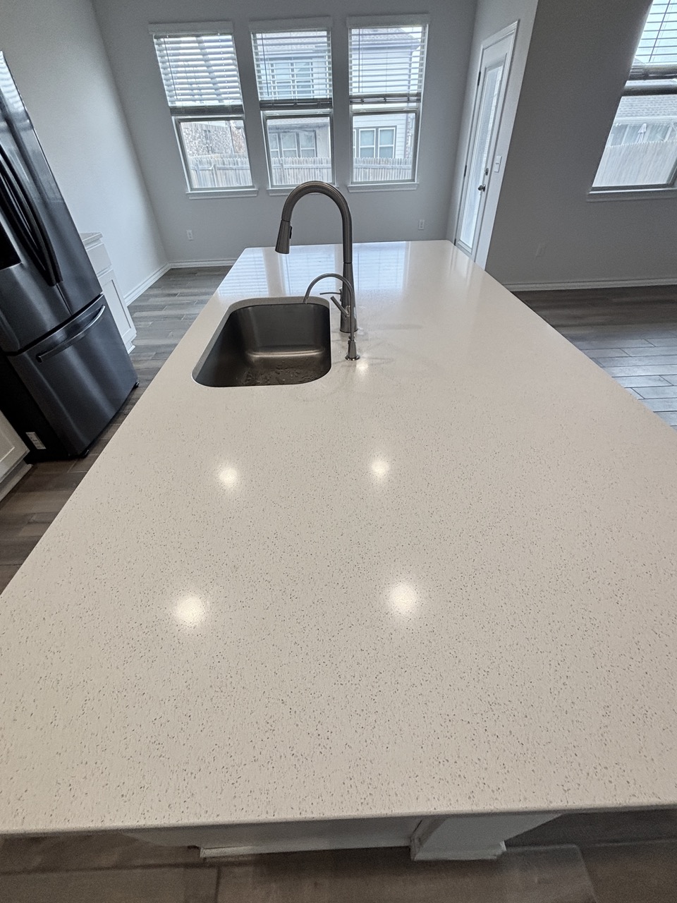 7606 Elk Grove Path Austin, TX 78754 - Photo 10 of 40 Kitchen view of light stone counters, freestanding refrigerator, a center island with sink, and dark wood-style floors