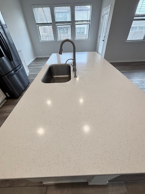 7606 Elk Grove Path Austin, TX 78653 - Photo 10 of 40 Kitchen view of light stone counters, freestanding refrigerator, a center island with sink, and dark wood-style floors