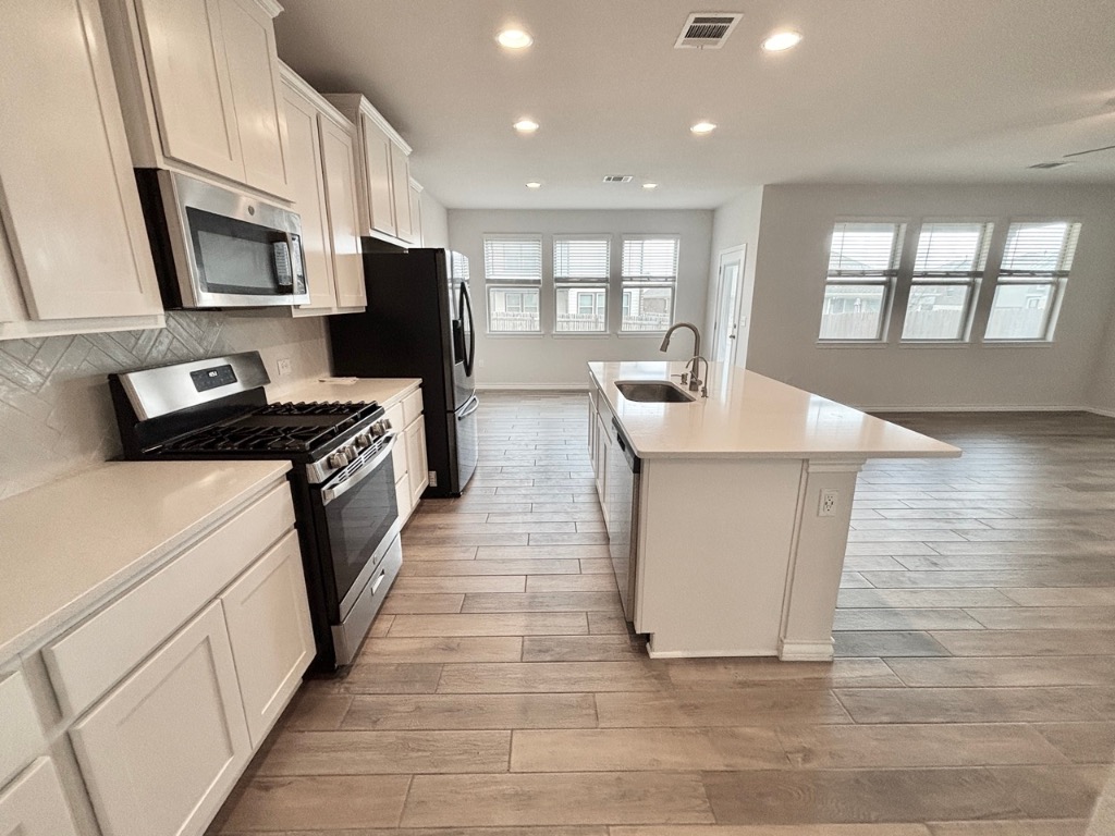 7606 Elk Grove Path Austin, TX 78653 - Photo 39 of 40 Kitchen with appliances with stainless steel finishes, an island with sink, recessed lighting, open floor plan, and white cabinets