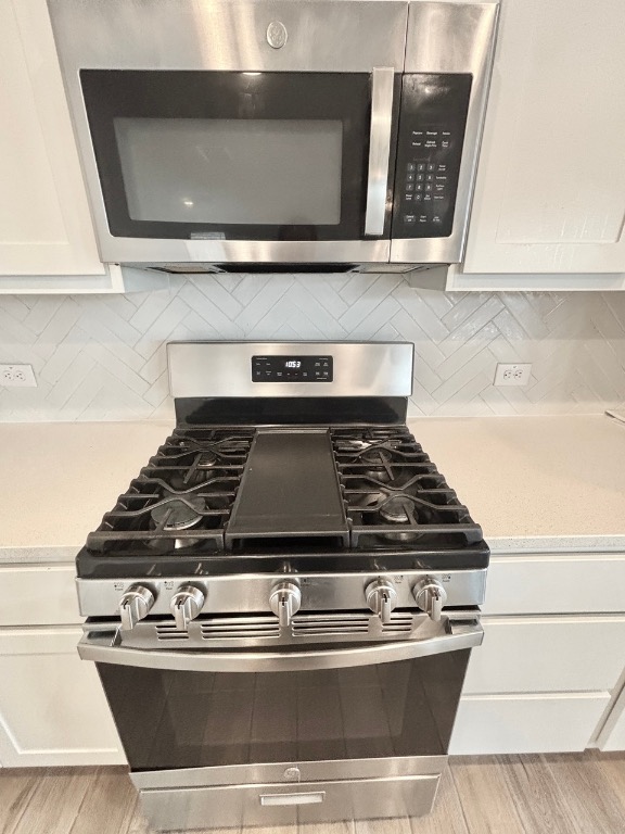7606 Elk Grove Path Austin, TX 78653 - Photo 12 of 40 Kitchen view of stainless steel appliances, white cabinets, light wood-style flooring, and backsplash