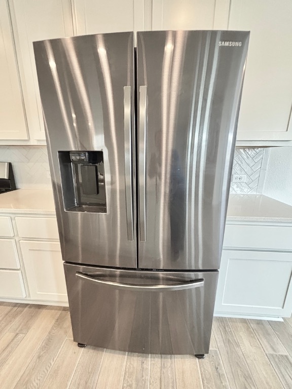 7606 Elk Grove Path Austin, TX 78653 - Photo 13 of 40 Kitchen view of stainless steel refrigerator with ice dispenser, white cabinetry, decorative backsplash, light wood-style floors, and light stone counters