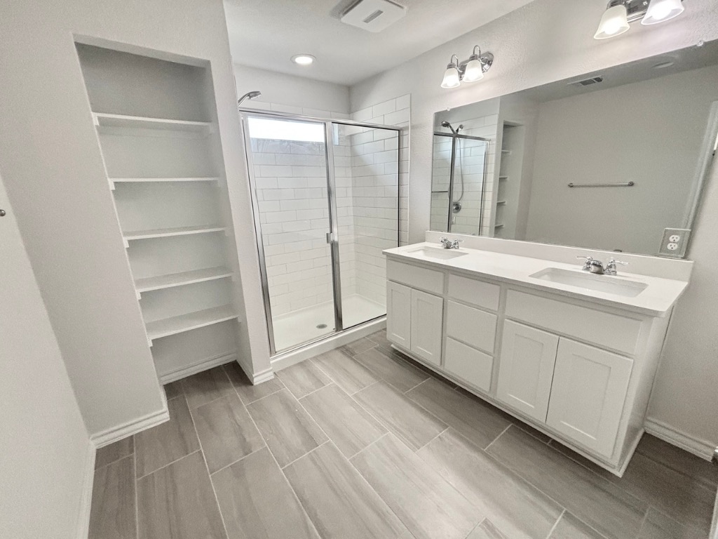 7606 Elk Grove Path Austin, TX 78653 - Photo 20 of 40 Full bathroom with double vanity, a shower stall, wood finish floors, and a spacious closet