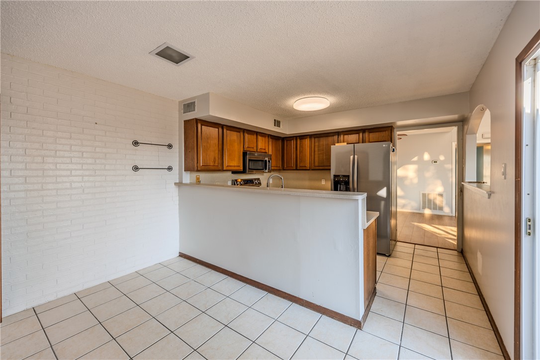 2002 South Lubbock Street Brenham, TX 77833 - Photo 13 of 26 Kitchen featuring brown cabinetry, brick wall, light countertops, appliances with stainless steel finishes, and a textured ceiling